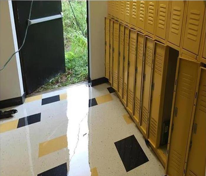 water puddling on tile floor, lockers, open exit door